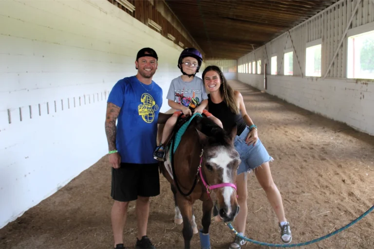 A camper rides a horse with two counselors helping out