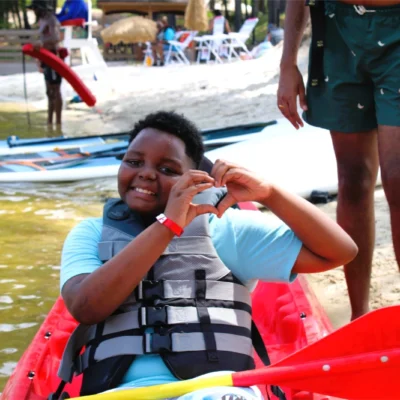A camper in a kayak makes a "heart" symbol with his hands
