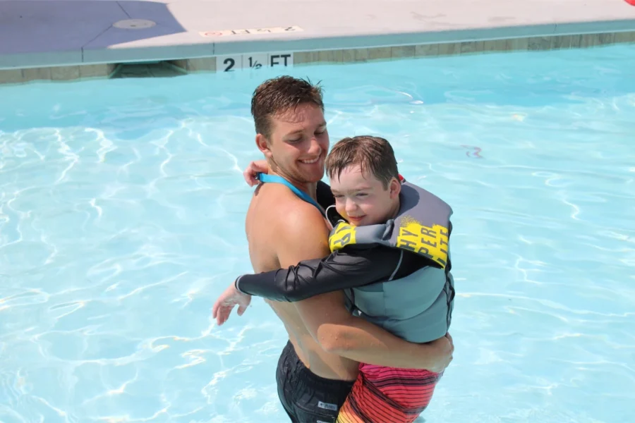 A counselor and camper hug in the zero entry pool