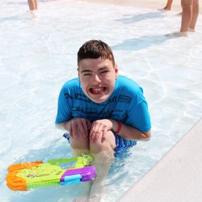 A camper smiles really big while playing in the zero entry pool