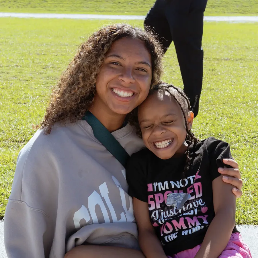 Two girls smile at the camera— on the left, a counselor, on the right, a camper